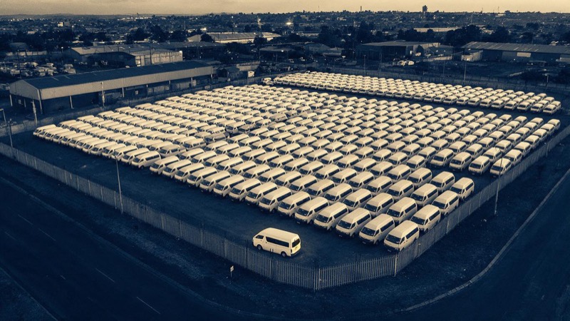 Dusk aerial of a large van depot near Johannesburg with hundreds of white vans parked in neat rows and a single van parked apart near the perimeter fence