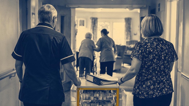Entrance hall of a care home with a polished floor, a reception desk and a vase of flowers in morning light, no one in sight