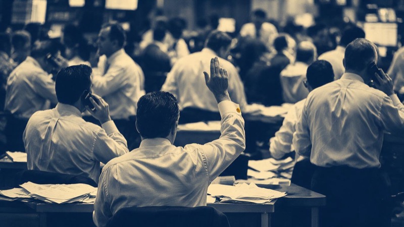 A long bank dealing room at midday in Singapore with chairs pulled up to rows of desks, lit by even white light