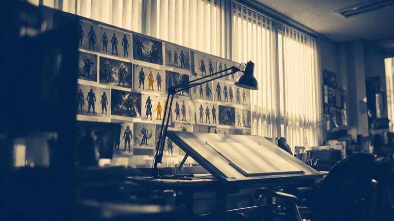 Concept paintings of fantasy characters pinned in rows along the wall of a Seoul game studio, afternoon light through tall blinds across an empty drawing desk