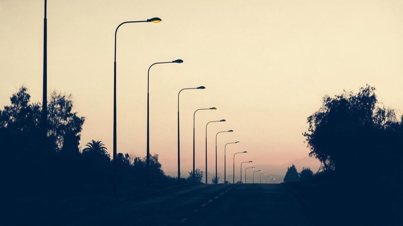 A long avenue of street lamps fading out one by one at dawn, an empty road leading toward a pale pink horizon in Santiago