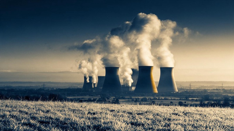Cooling towers steaming at dawn over a river plain in the English Midlands, seen from a field of frosted grass
