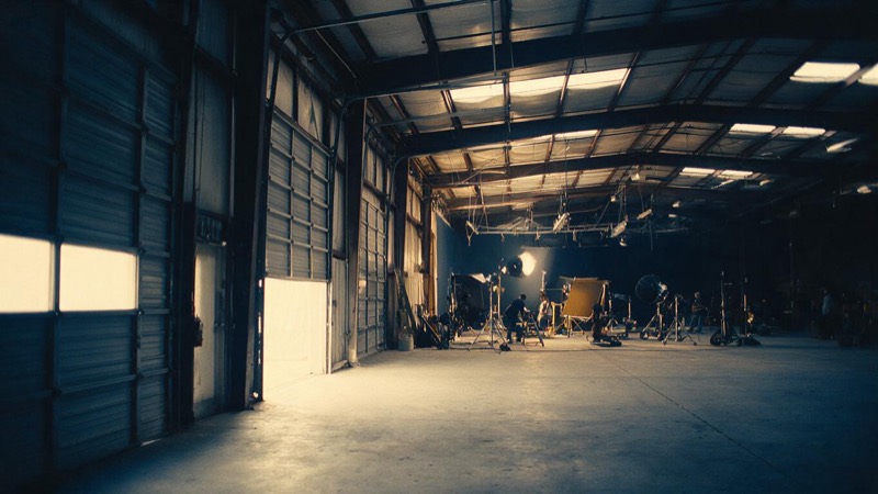 Empty warehouse converted into a film studio with tall roller doors and a bare concrete floor, light falling through skylights
