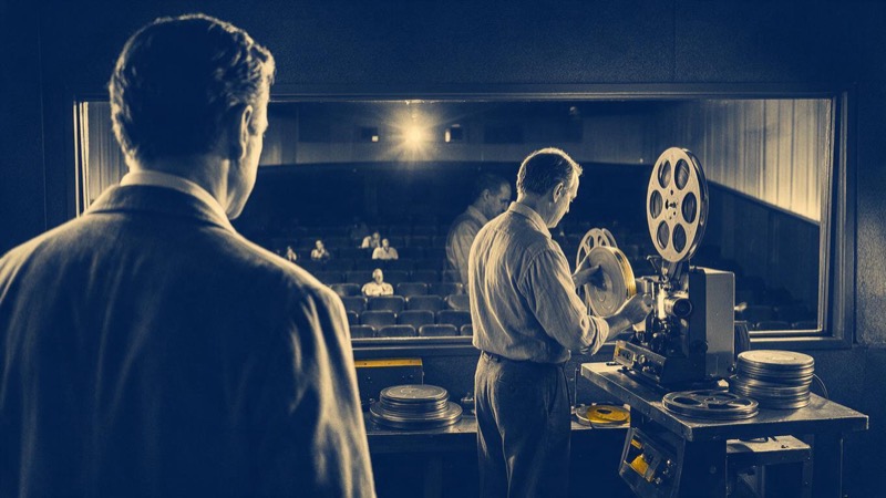View from the stage of an empty cinema auditorium, rows of seats rising toward the projection window in dim house lights