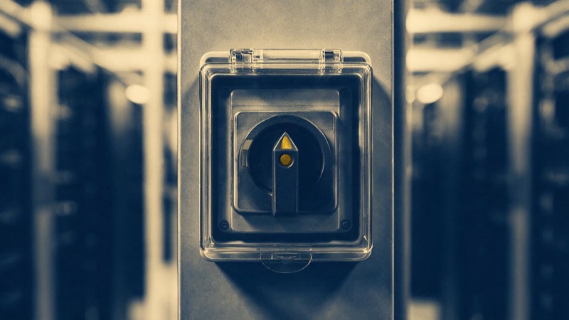 Close-up of a red emergency power-off switch behind a clear plastic cover on a wall in a server hall