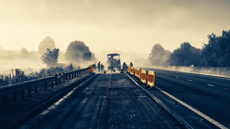 A section of motorway with roadworks and orange barriers on a misty morning, a paving gang at work in the distance