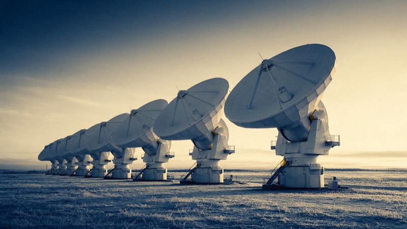 A row of large white satellite ground-station dishes on a flat plain in northern Sweden under a pale dawn sky, frost on the grass