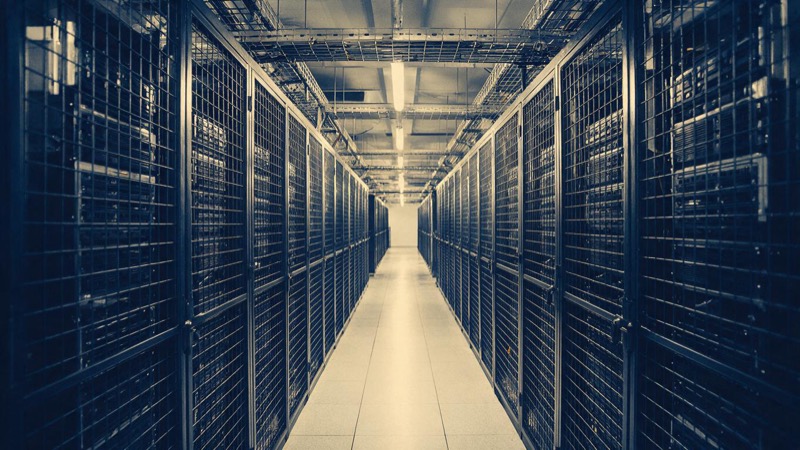 Rows of servers behind steel mesh cages in a colocation hall in Johannesburg, cool white light along the aisle and cable trays overhead