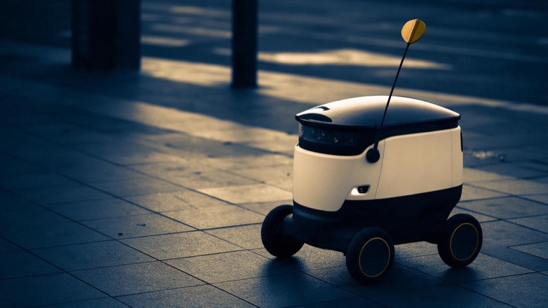 a delivery robot on an empty city pavement at dawn