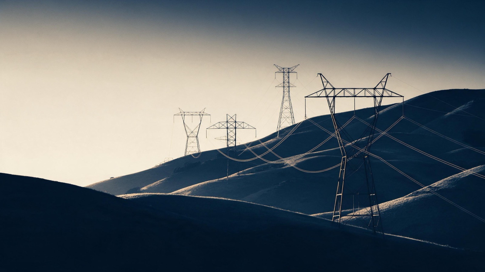 high-voltage pylons crossing hills at dusk, cables catching the light