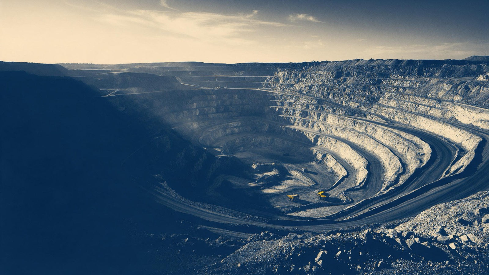 a vast open-pit mine terraced like an amphitheatre, haul trucks small at the bottom