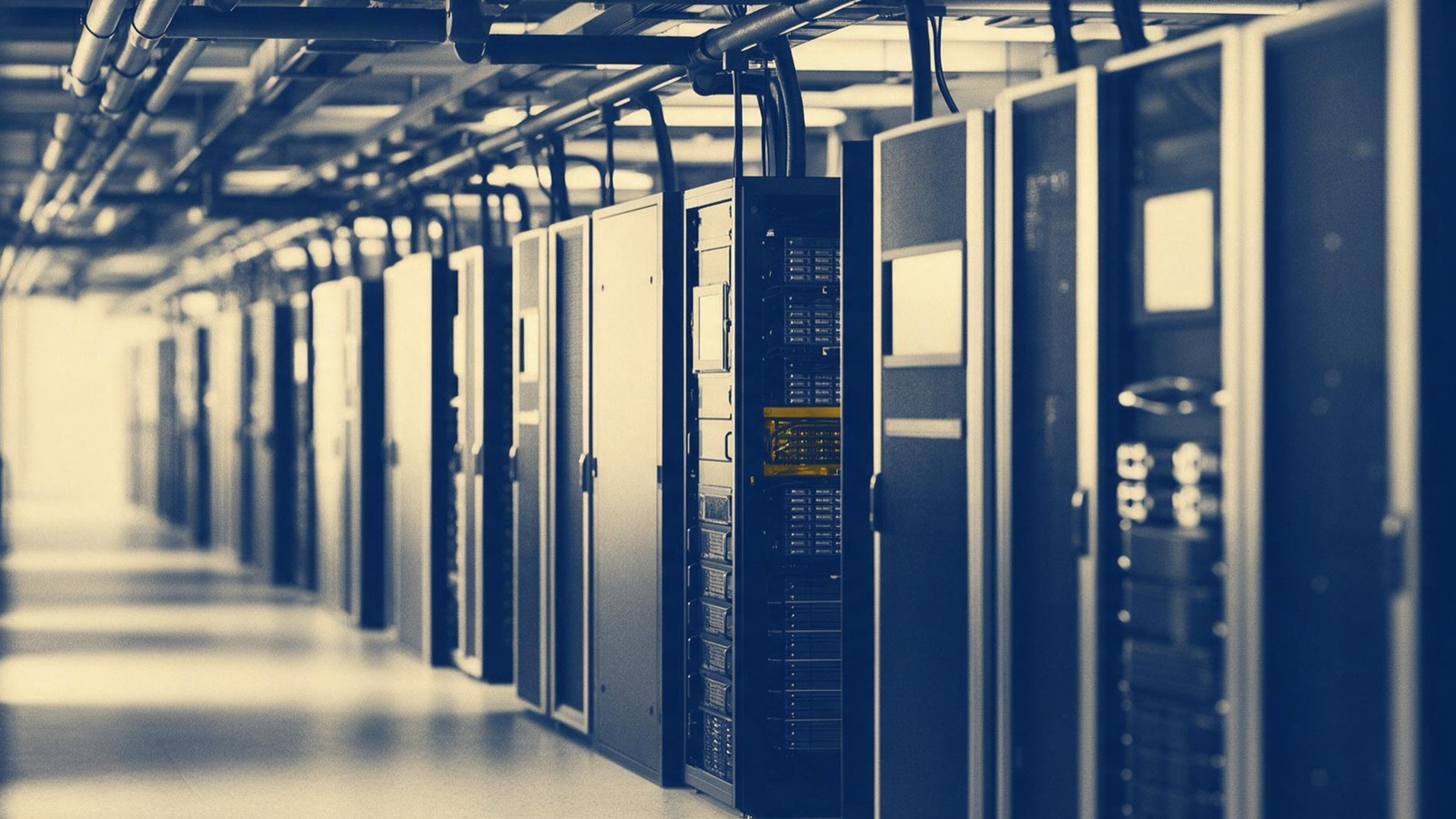 a supercomputer hall with long aisles of cabinets and cooling pipes