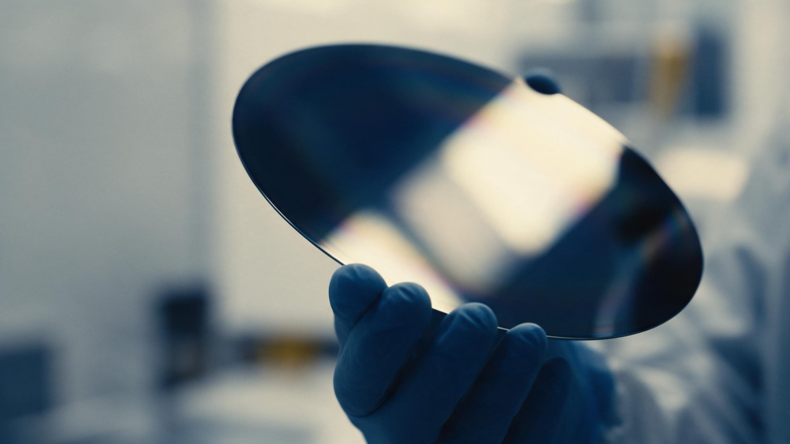 a silicon wafer held in a gloved hand in a clean room, iridescent surface