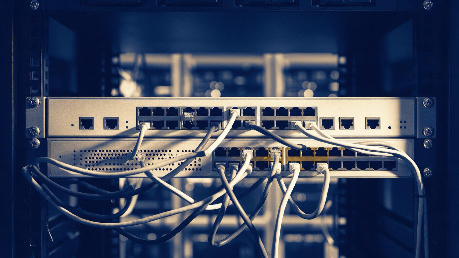 An unbranded network firewall and switch mounted in a rack, rows of ports and tangled patch cables photographed close under hard white light