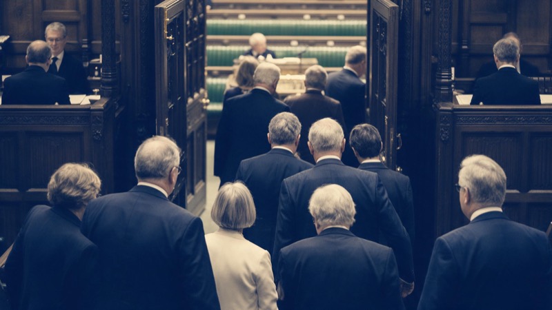 Rows of empty leather benches in an old legislative chamber, dust drifting in a shaft of light from a high window
