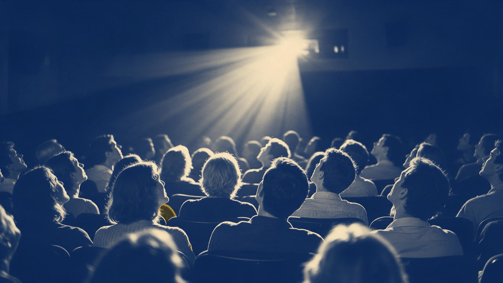 Rows of cinema-goers seen from behind in a dark auditorium, heads lifted toward a shaft of projected light