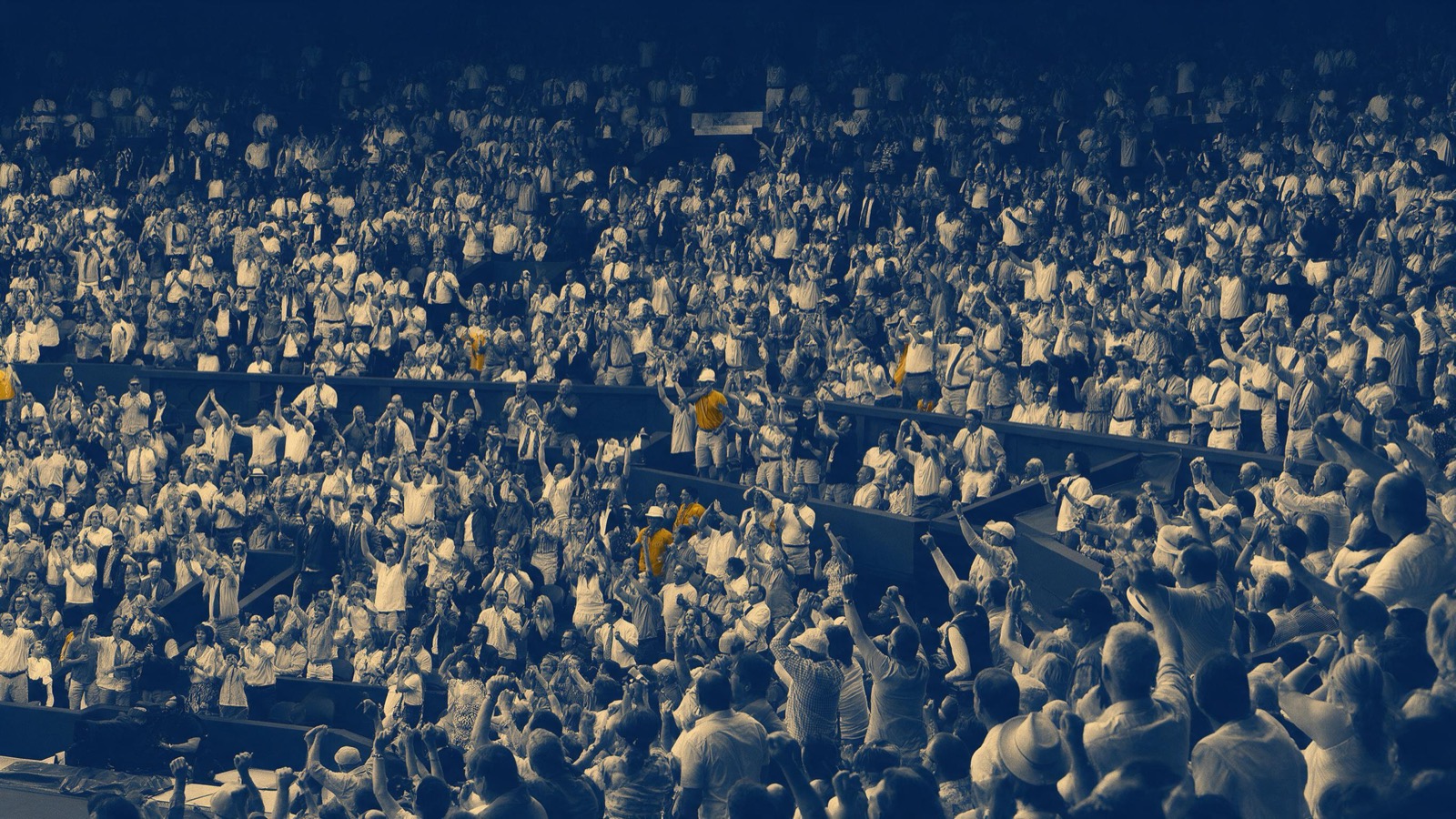 A vast stadium crowd seen from far above, thousands rising to their feet at once at the moment the ball hits the net