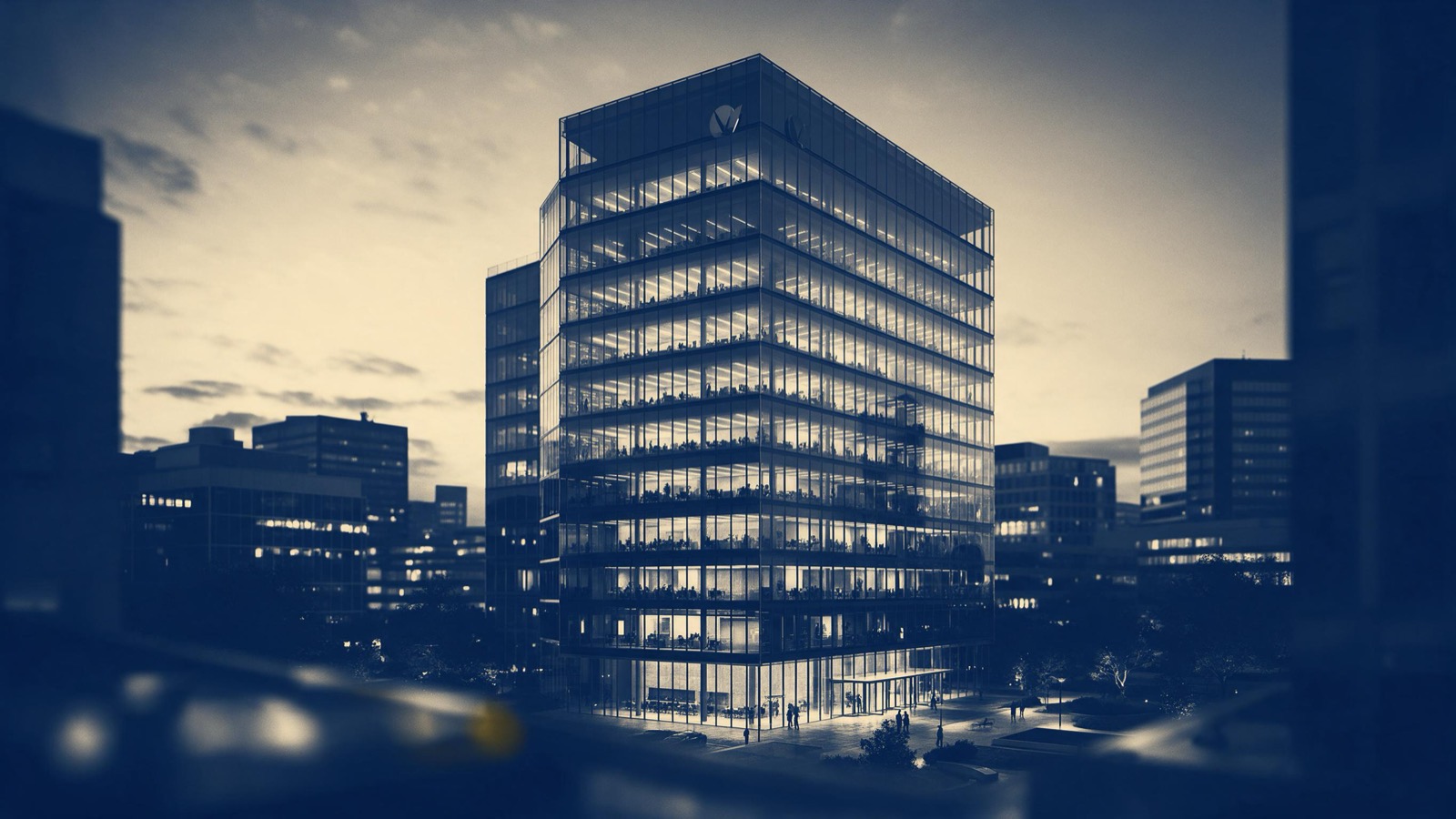 A glass headquarters tower of a large company standing in a business district at dusk, lit floors above a quiet plaza