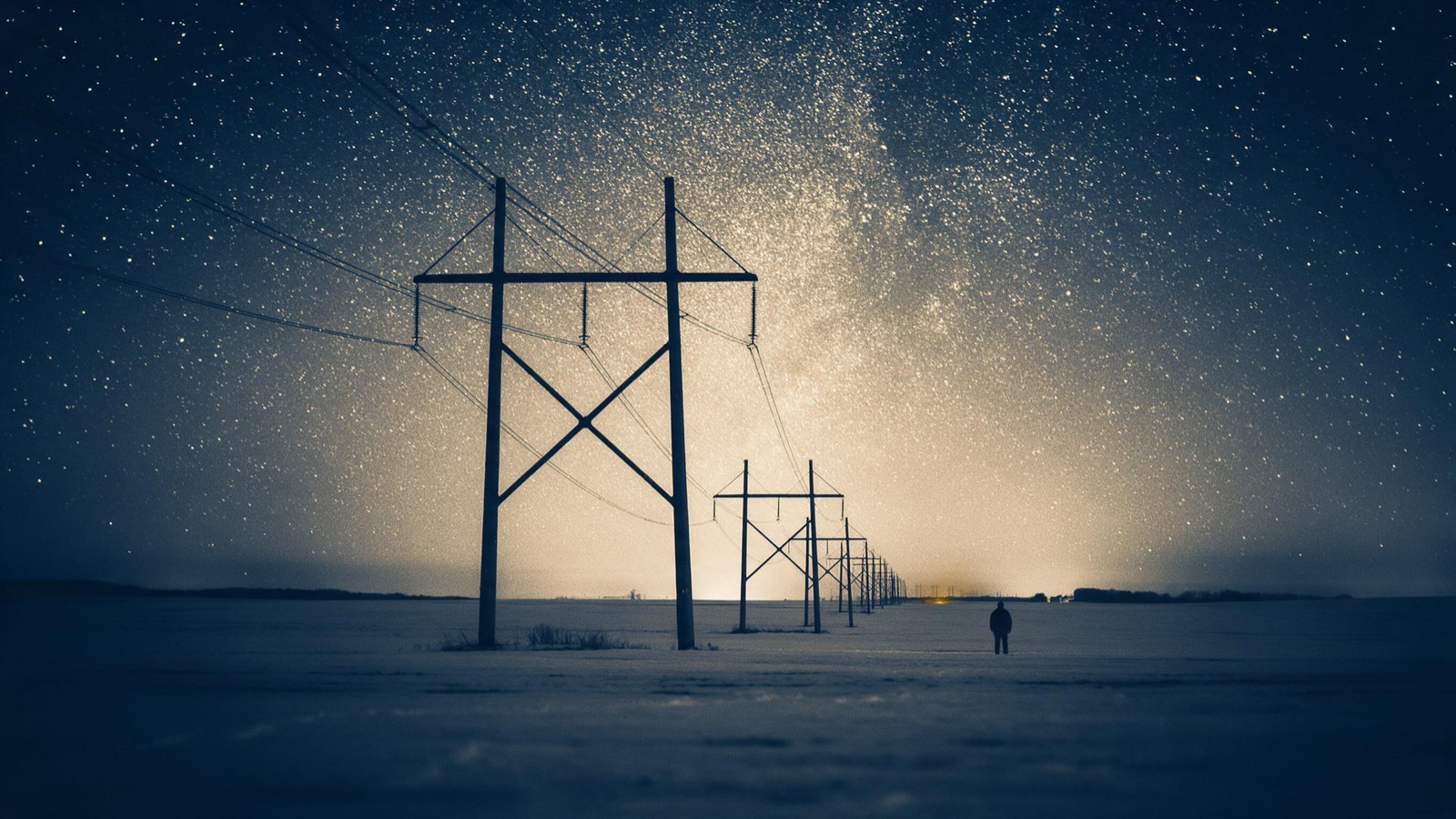 Green aurora over a line of high-voltage pylons at night, the towers silhouetted against the shimmering sky above a frozen field